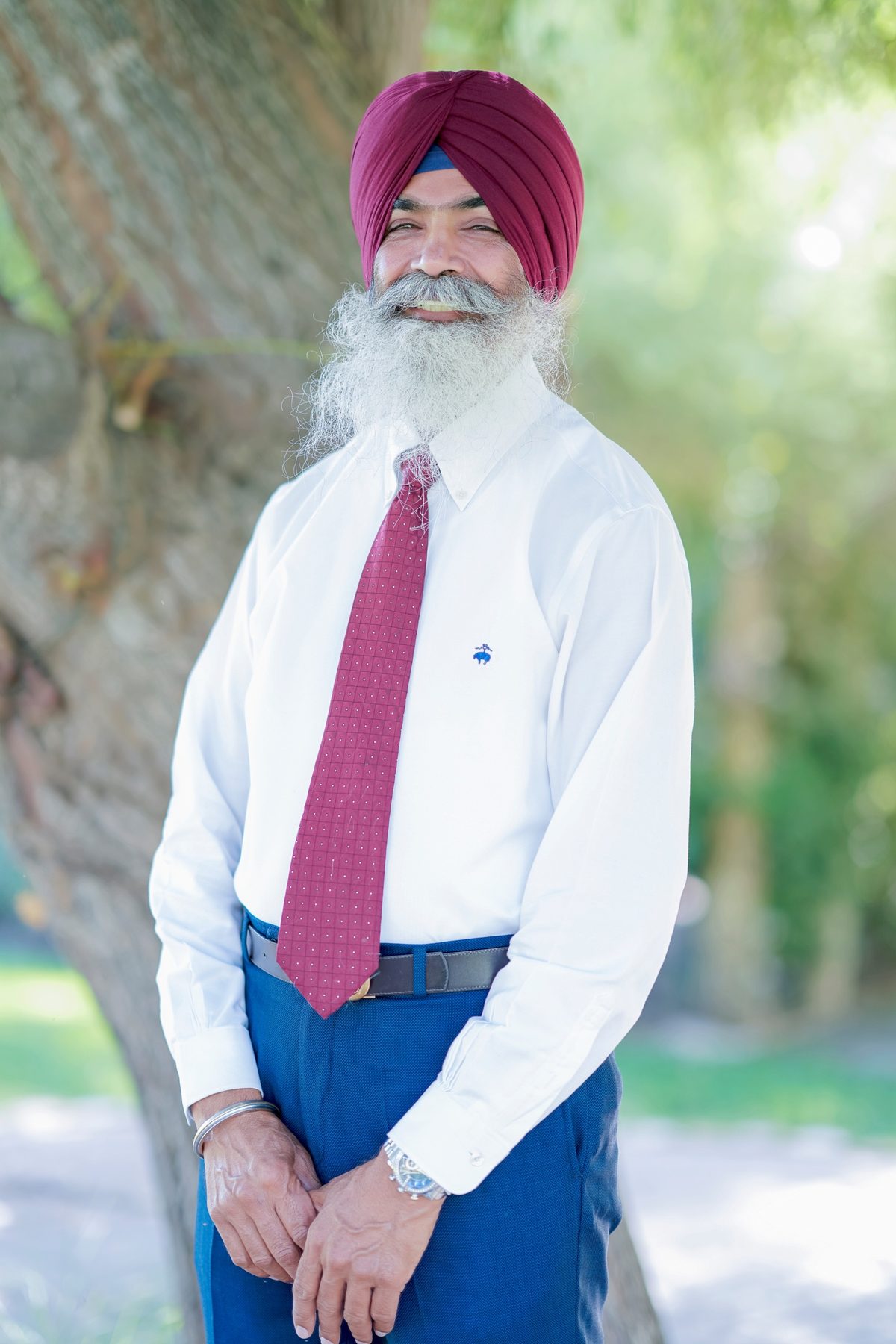 Gurjant Singh Khosa in a white shirt and tie, standing under a tree
